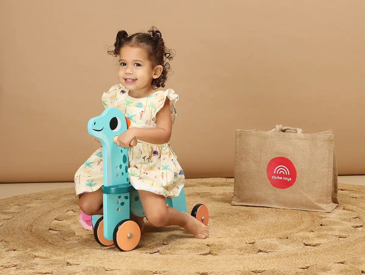 Menina pequena sentada em carrinho de dinossauro da Club Toys