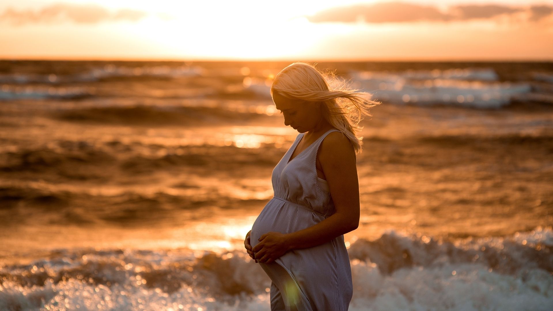 Mulher grávida posando no pôr do sol na praia.