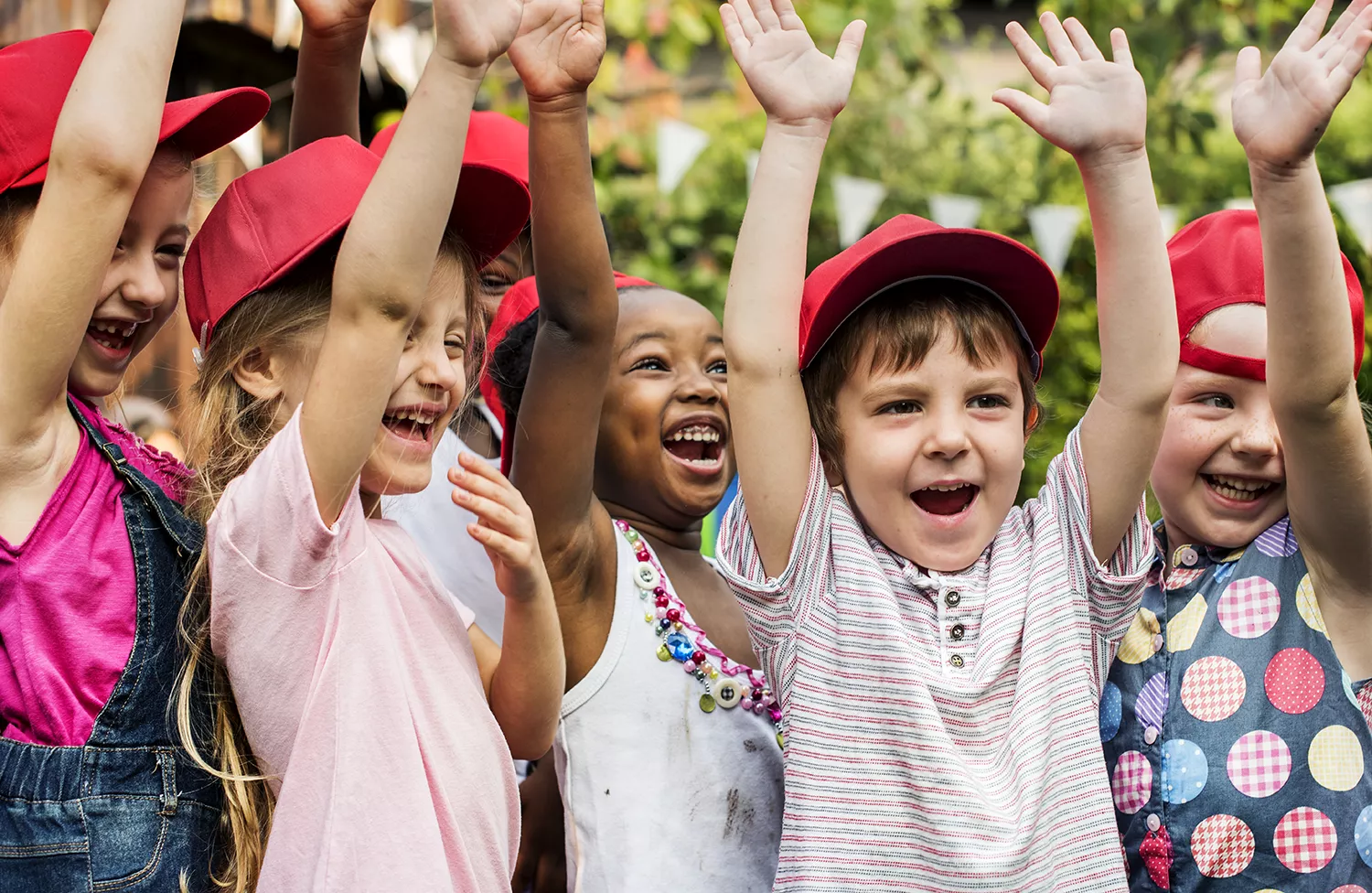 Crianças com as mãos para cima, sorrindo, todas de bonés vermelhos
