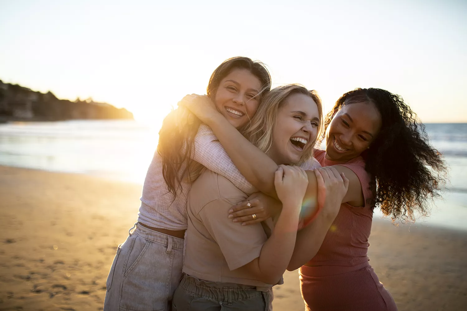 3 mulheres rindo e se abraçando na praia