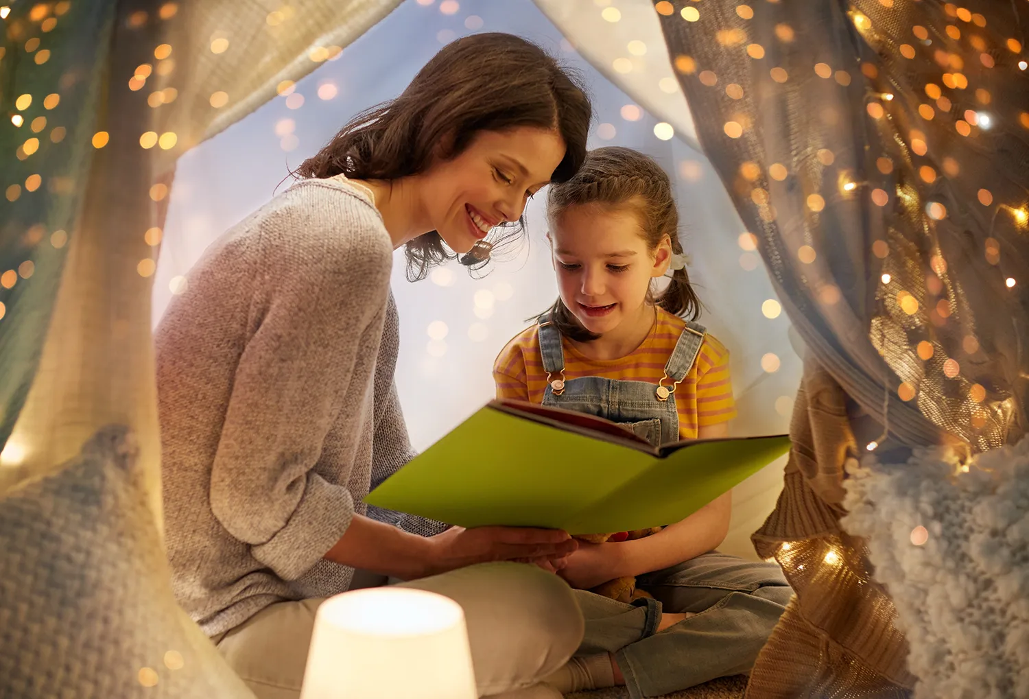 mãe lendo livro para filha pequena