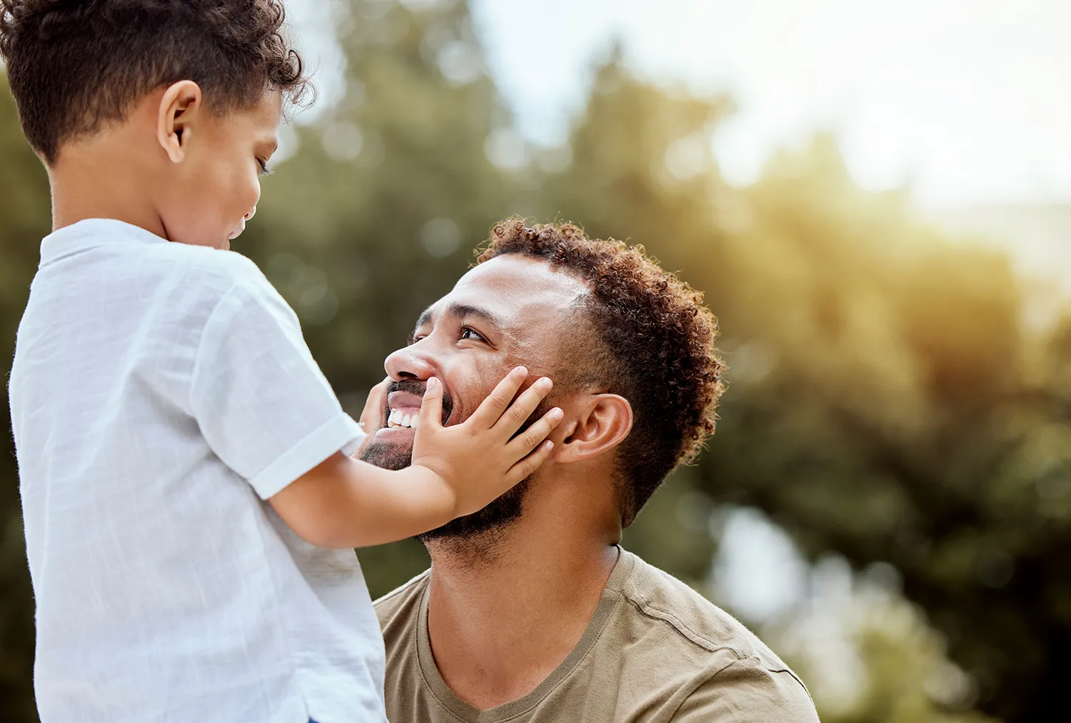 Pai agachado sorrindo para filho que coloca mãos em seu rosto