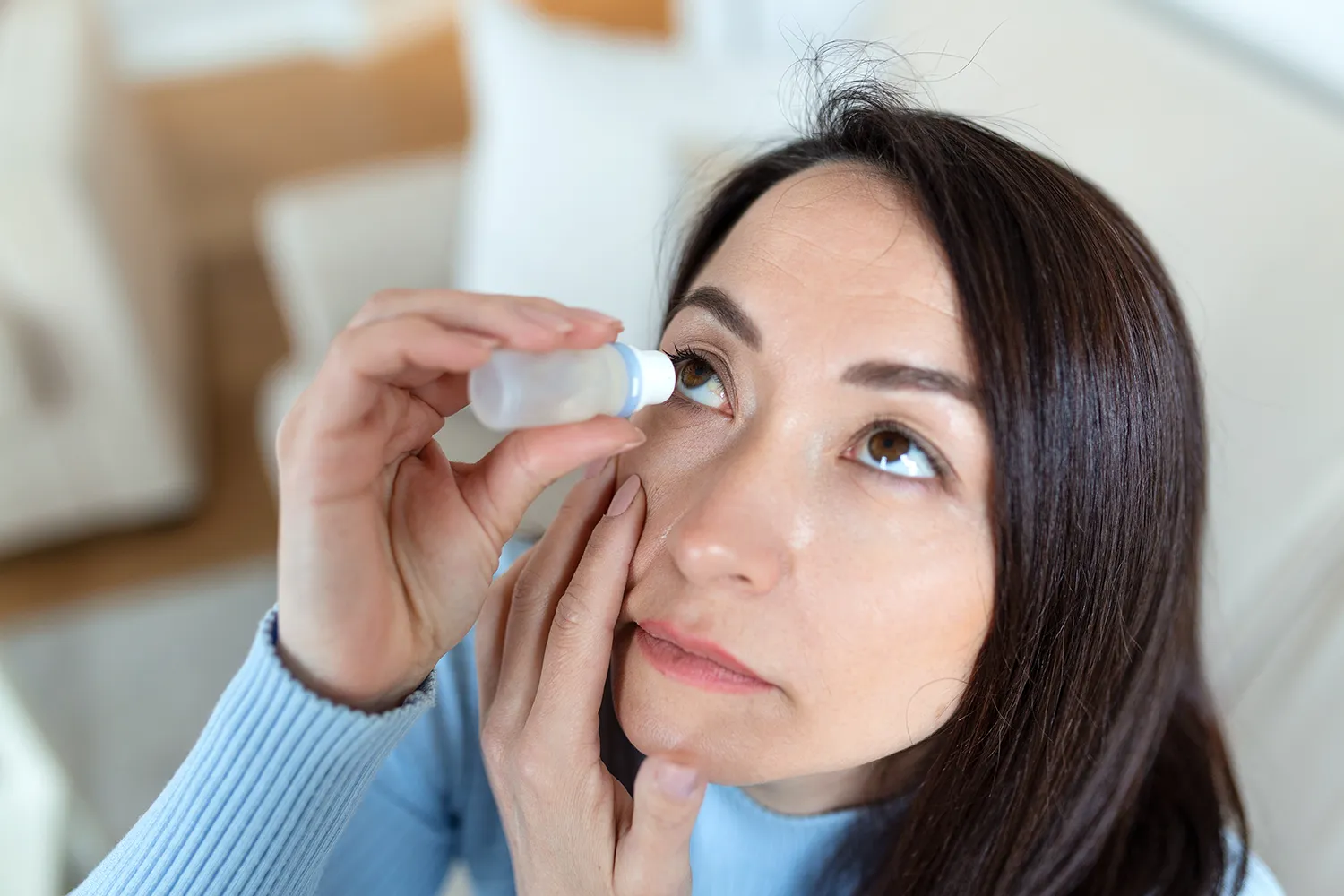 Mulher pingando colírio nos olhos secos e irritados, por causa da menopausa