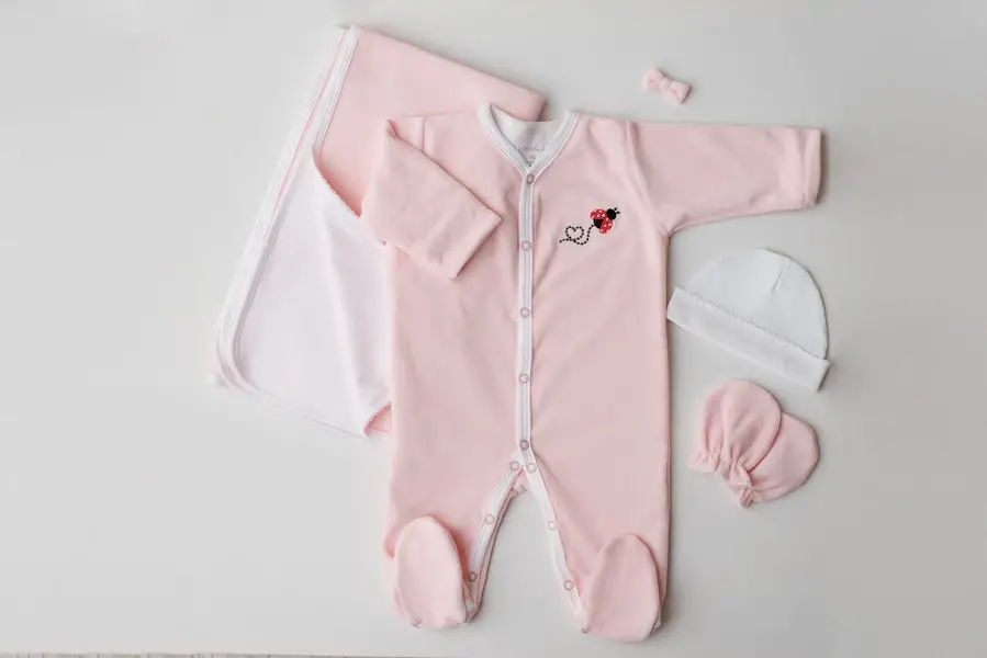 Pijama infantil de plush rosa com acessórios ao lado - lacinho, gorro e luva - Just Real Moms