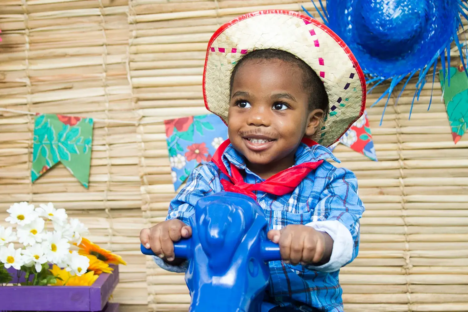 menino vestido de Festa Junina em cima de um brinquedo de cavalo azul