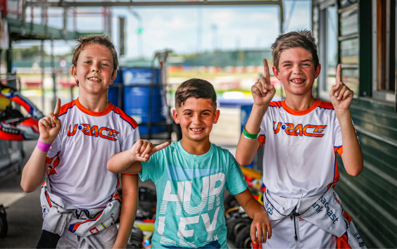 Three young Urace karting students smiling in the paddock